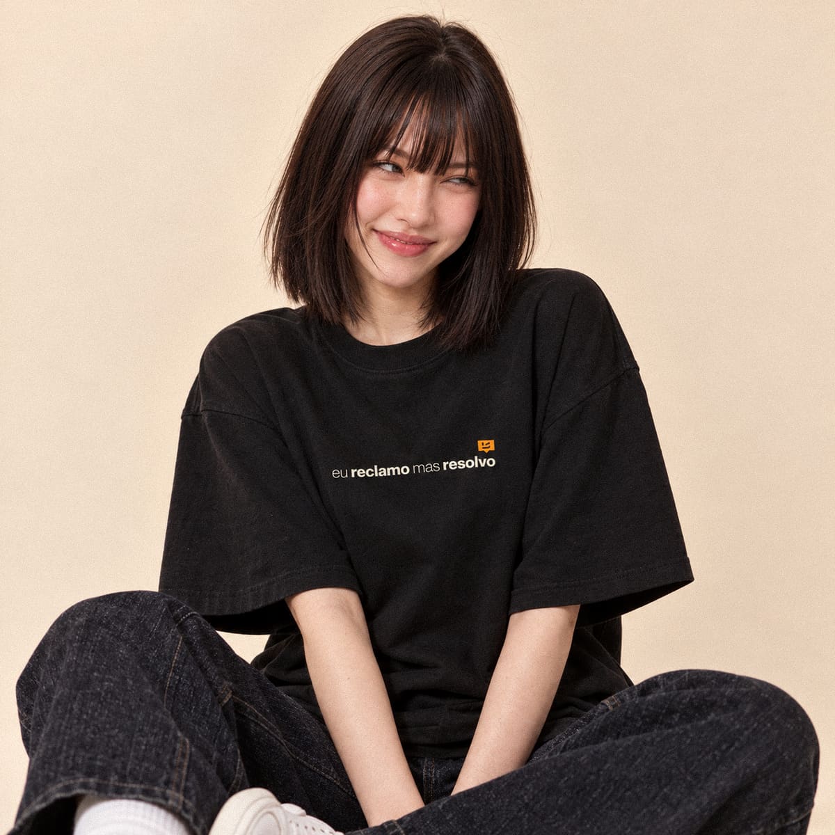 Modelo sorrindo, sentada no chão, com uma camiseta preta da BemDitto